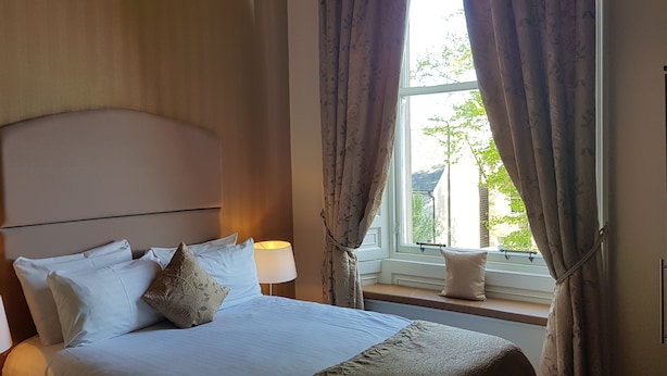 Une chambre à coucher avec un lit, deux lampes de chevet, une fenêtre avec des rideaux et une vue sur la verdure à l’extérieur.