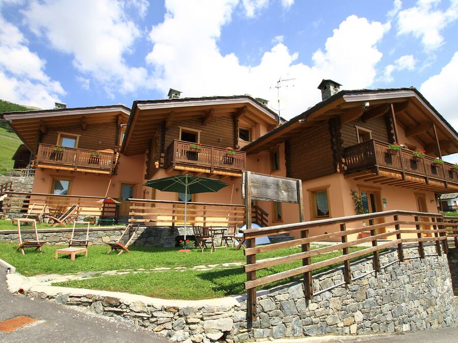Un edificio de estilo chalete con varios balcones, mobiliario exterior y un muro de contención de piedra.
