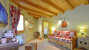 Una sala de estar acogedora con techo de madera, un sofá, una mesa de madera y una zona de cocina con mostrador y electrodomésticos.