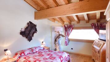 Un dormitorio con techo de madera, una cama con colcha estampada, una mesita de noche con lámpara y una ventana con cortinas.