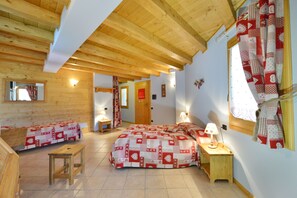Una habitación acogedora con techo de madera, una cama con colcha a cuadros rojos y blancos, un banco de madera y una mesita con lámpara.
