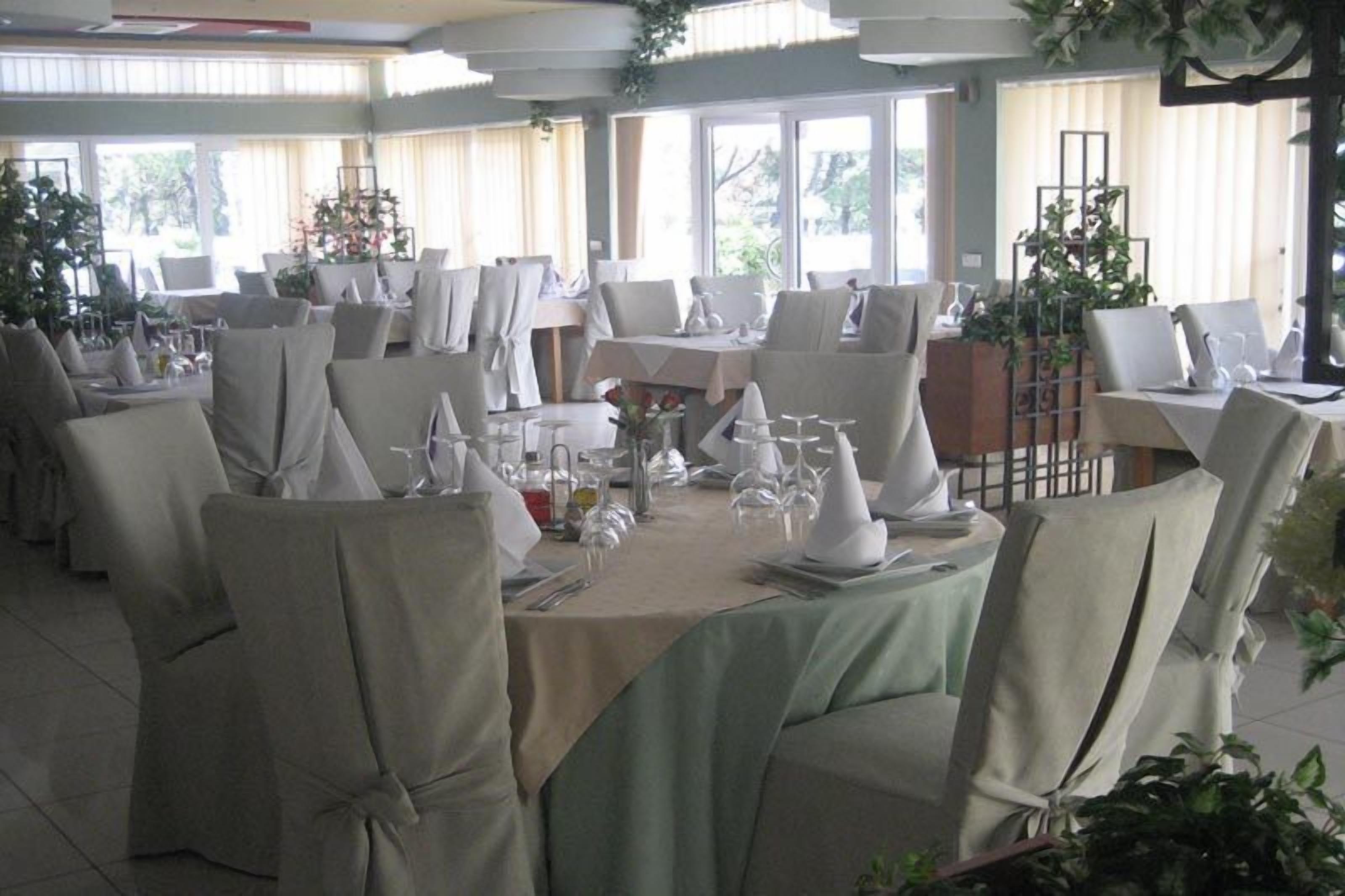 A banquet hall with round tables set for dining, covered with white tablecloths and chairs with white covers.