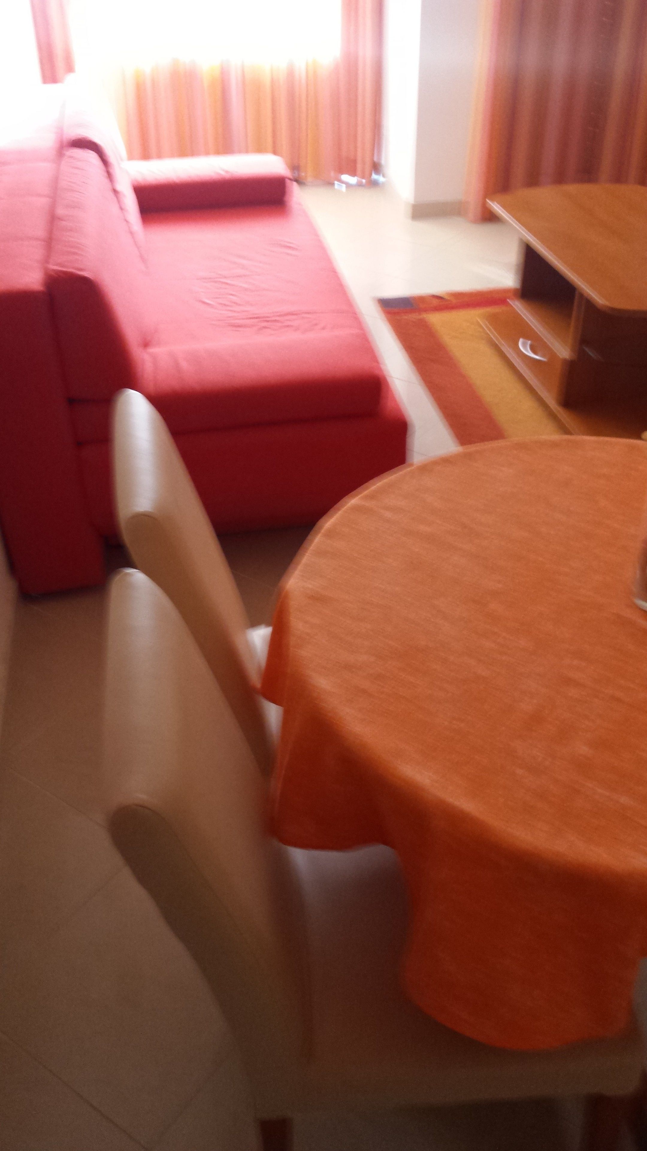 Een kamer met een rode bank, een houten eettafel met een oranje tafelkleed, en een witte stoel.