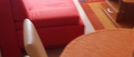A room with a red sofa, a wooden dining table with an orange tablecloth, and a white chair.