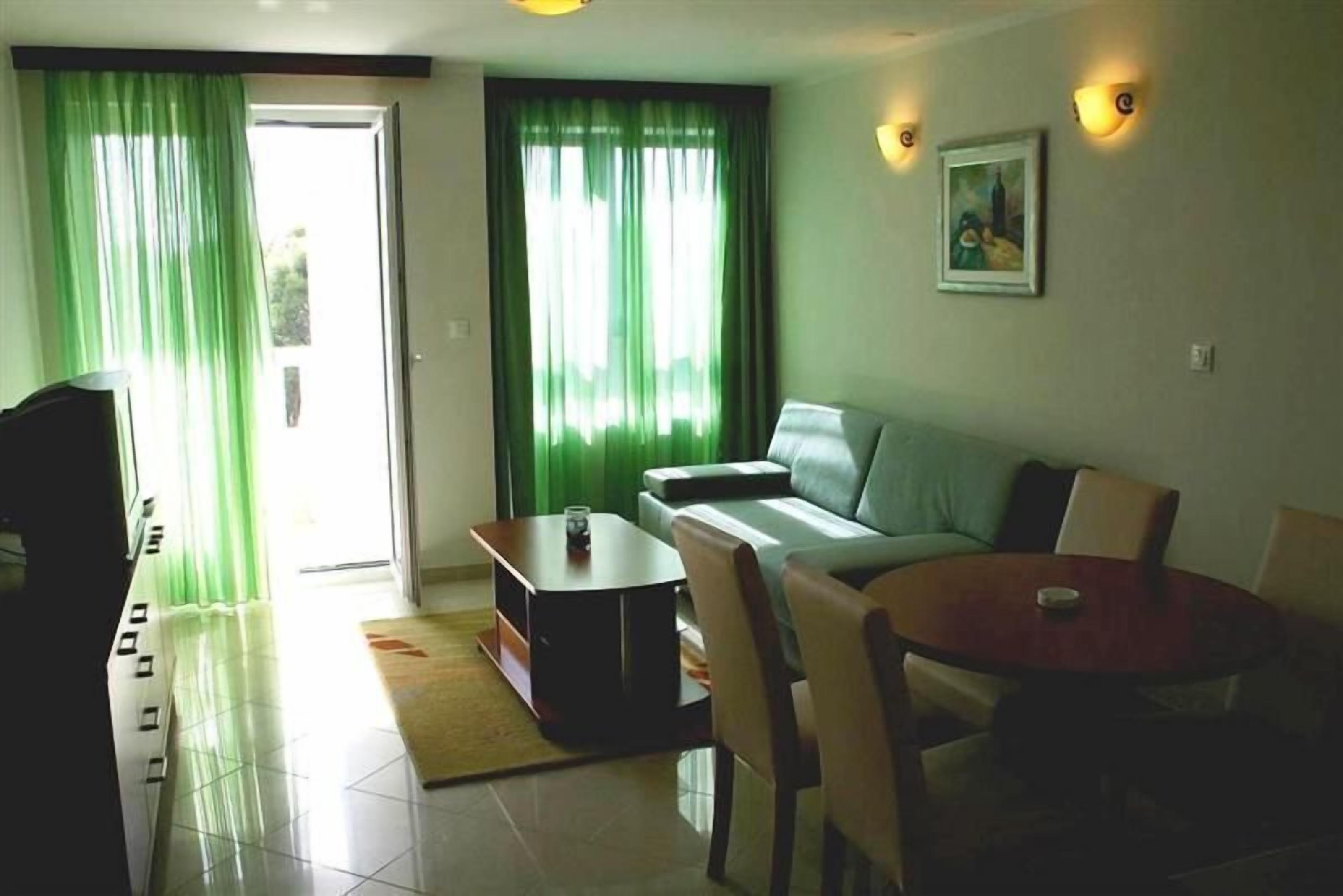 Una sala de estar con sofá, mesa de centro y televisor. Hay una puerta que da al exterior y un cuadro en la pared.