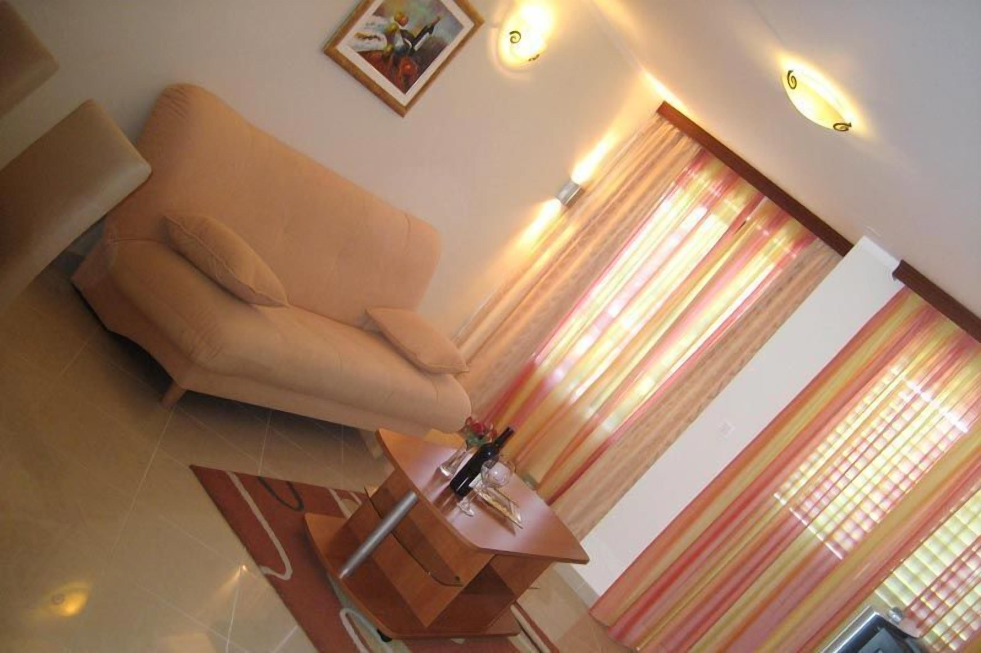 A living room with a beige sofa, a small wooden side table with a bottle and glass, and a painting on the wall.