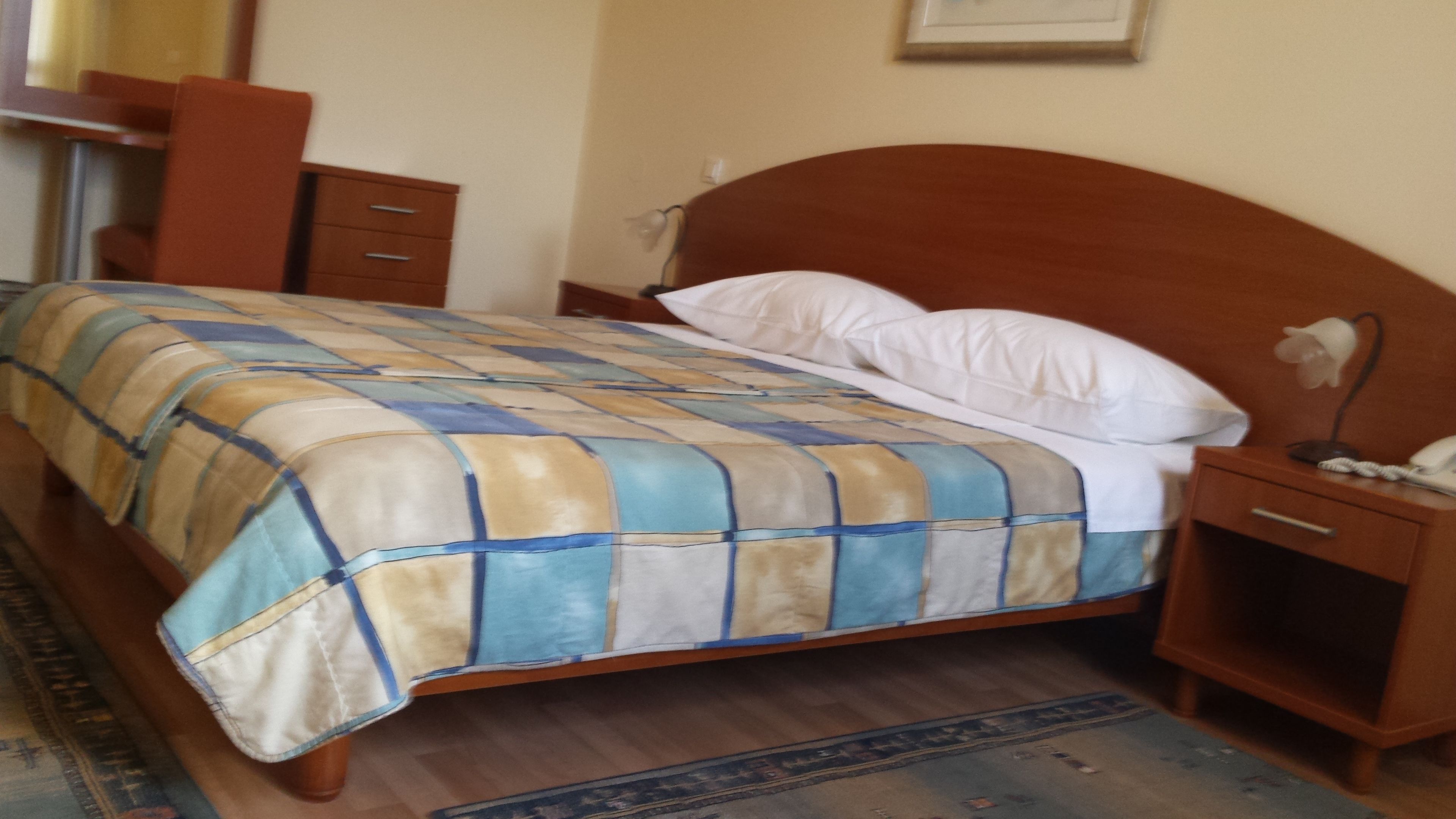 Ein Bett mit karierter Bettdecke, ein Holzkopfteil, ein Nachttisch mit Lampe und ein Beistelltisch mit Telefon.