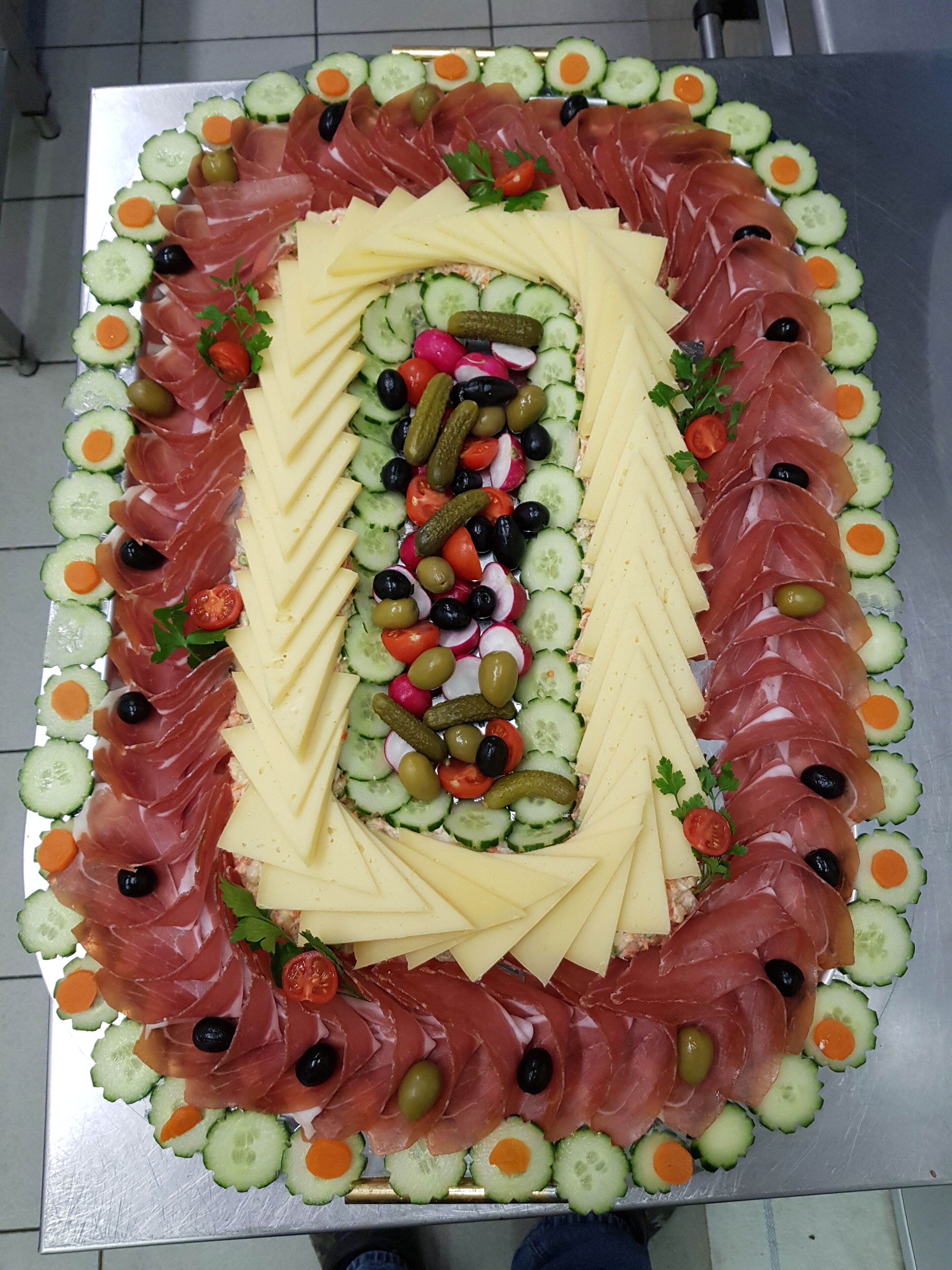 A rectangular platter of assorted deli items including sliced meats, cheeses, and vegetables.