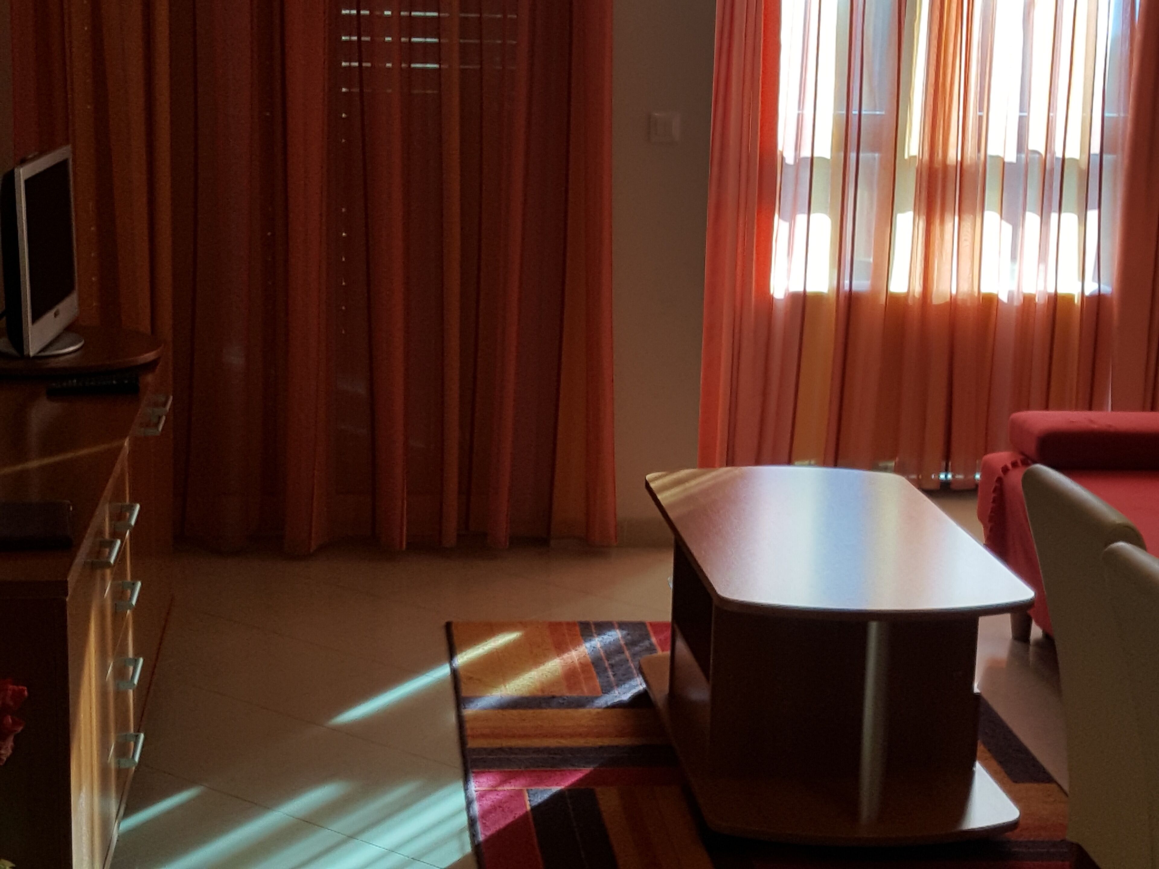 A room with a flat-screen TV on a wooden cabinet, a round table, and a red sofa.