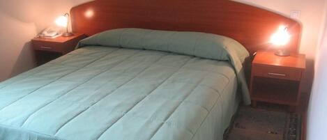 Una cama bien hecha con una colcha verde y almohadas, con mesitas de noche de madera y lámparas a cada lado.