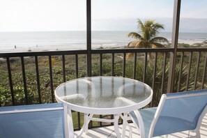 Mesa de vidrio con dos sillas en un balcón con vista a la playa.