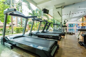 Une salle de sport équipée de tapis de course, d’appareils de musculation et d’un grand miroir.