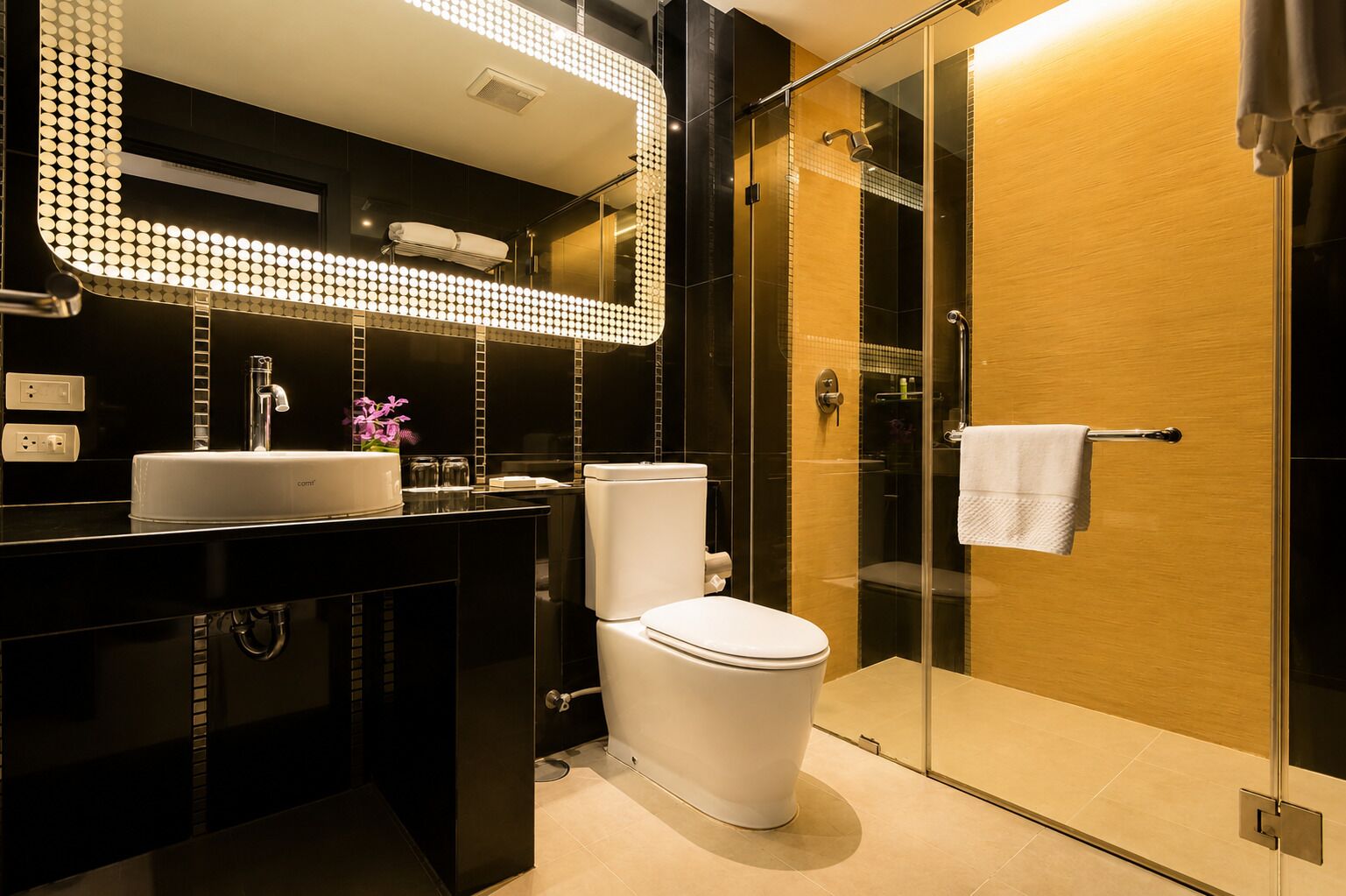 Ein modernes Badezimmer mit schwarzem Waschtisch, weißem Waschbecken und WC, einer Duschkabine aus Glas und einer Holztür.