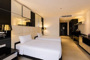 A hotel room with two beds, a desk, a mirror, and a kitchenette. - Nova Platinum Hotel (Pattaya)