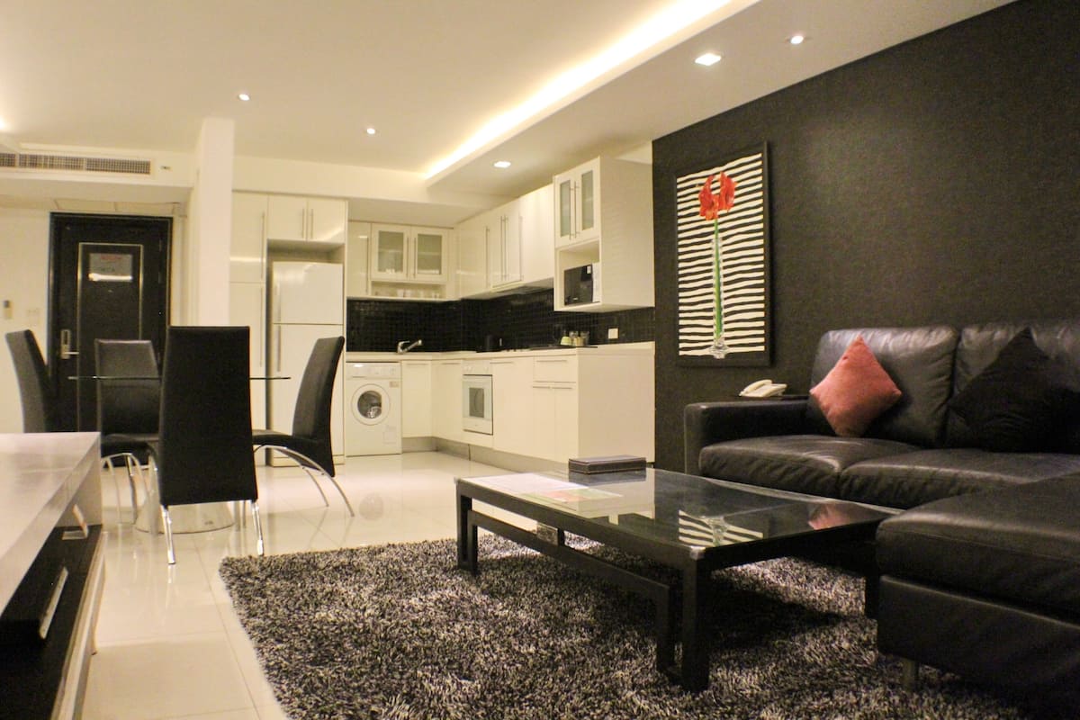Una sala de estar moderna con un sofá de cuero negro, una mesa de centro de vidrio y una alfombra blanco y negro.