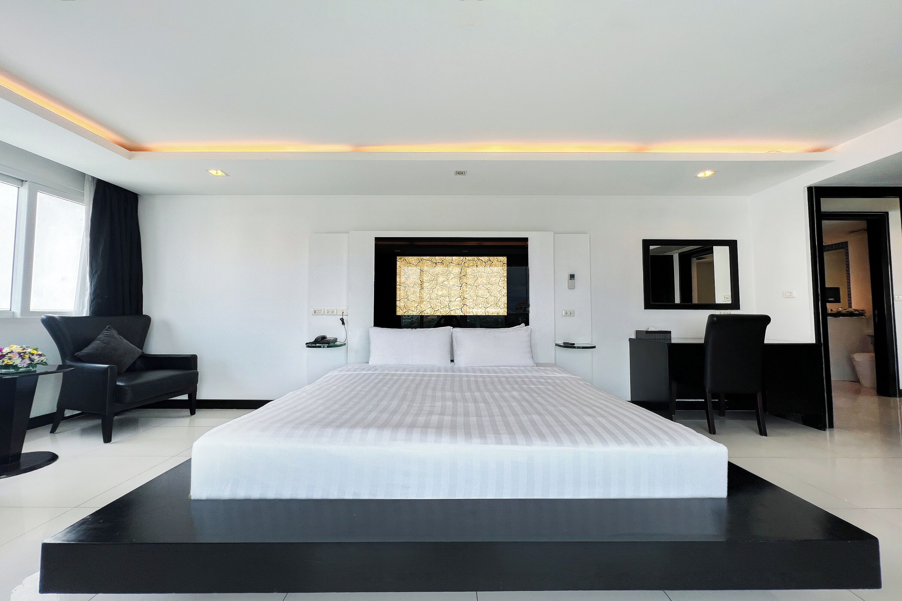 A modern hotel room with a large bed, a desk, a chair, and a window.