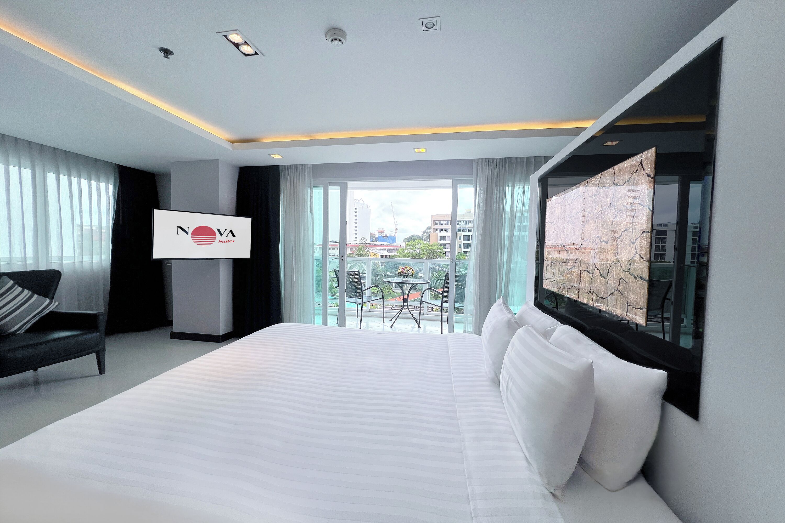 Ein Hotelzimmer mit einem Bett, einem Sessel, einem Tisch mit Stühlen, einem großen Fenster und einem Schild mit dem Hotelnamen.