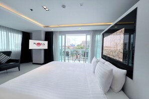 A hotel room with a bed, a chair, a table with chairs, a large window, and a sign with the hotel's name. - Nova Suites Pattaya by Compass Hospitality (Pattaya)