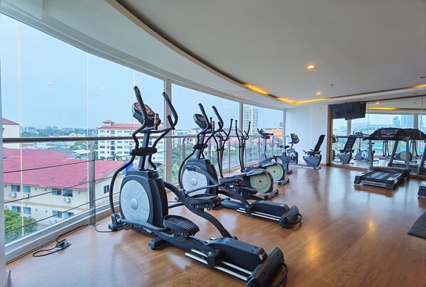 A gym with multiple exercise machines, large windows, and a city view. - Nova Suites Pattaya by Compass Hospitality (Pattaya)