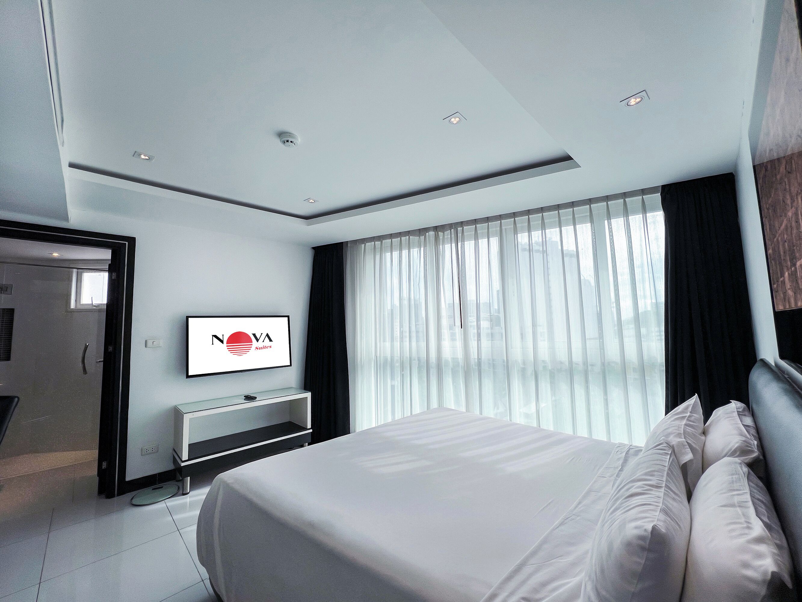 Ein modernes Hotelzimmer mit einem Bett, einem an der Wand befestigten Fernseher und einem großen Fenster mit Vorhängen.