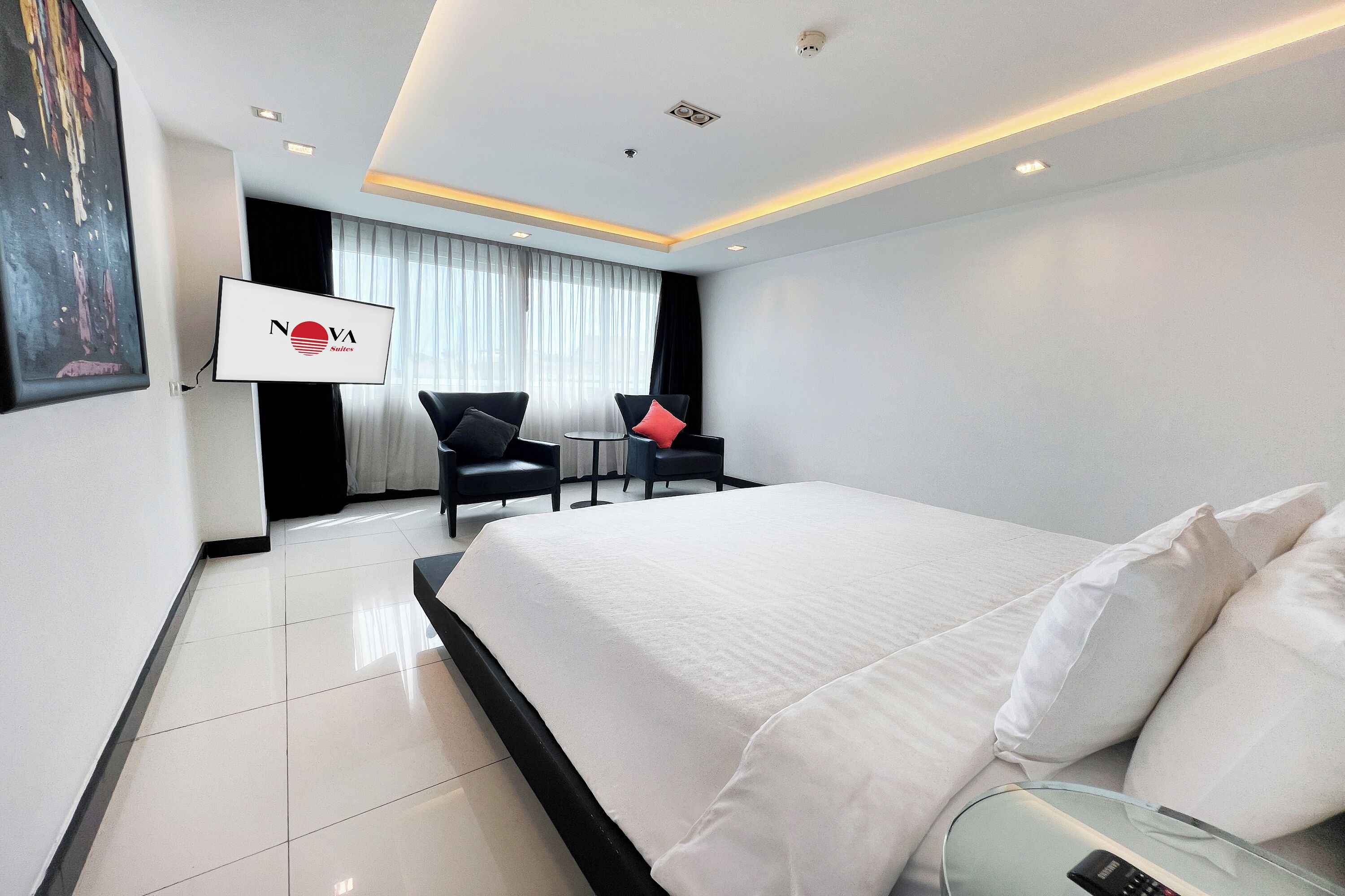 Ein Hotelzimmer mit einem großen Bett, zwei Sesseln, einem Fernseher und einem Gemälde an der Wand.