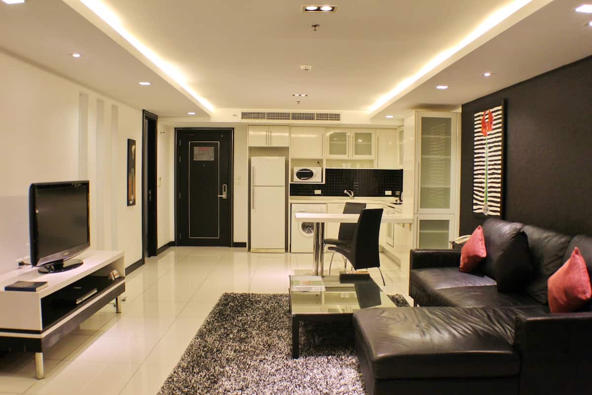 Un moderno salón con televisión de pantalla plana, un sofá de cuero negro con cojines rosa y una mesa de centro de vidrio.