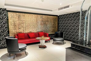A modern living room with a red sofa, two armchairs, a small round table, and a decorative wall with a crackled pattern. - Nova Suites Pattaya by Compass Hospitality (Pattaya)