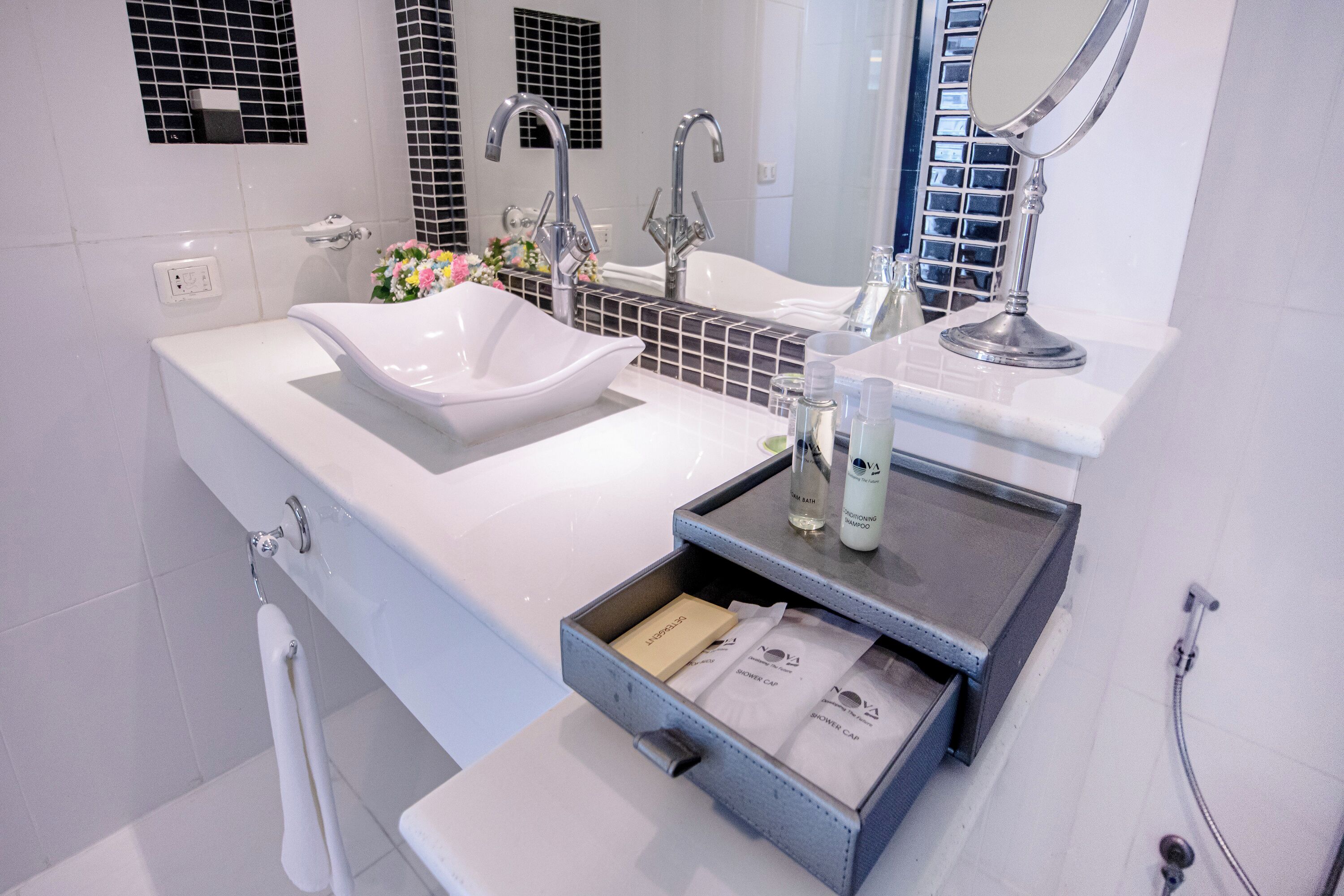 A modern bathroom with a white sink, two faucets, a mirror, and a shower area.