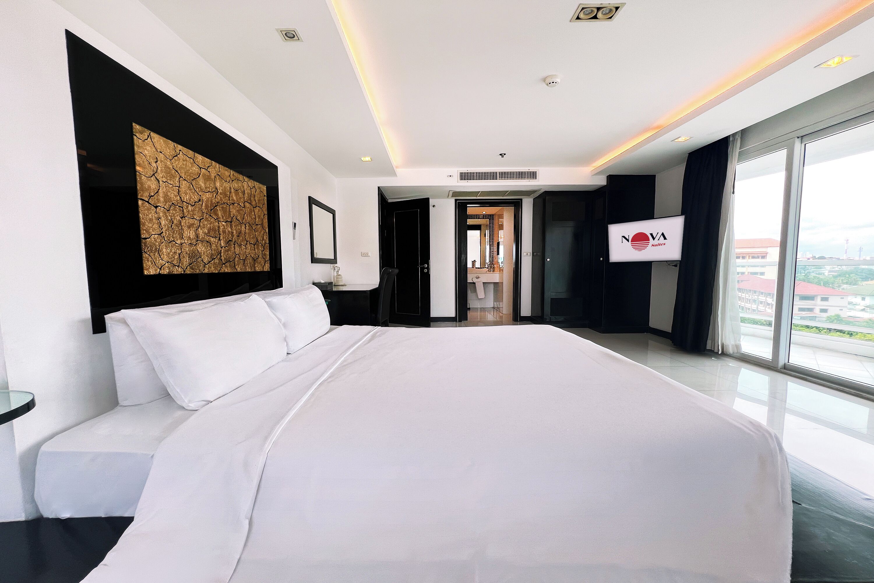 A modern hotel room with a large bed, a view of the city, and a sign for NOVA Suites.