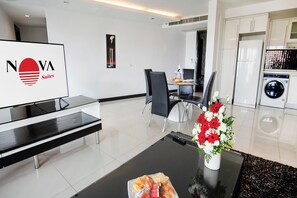 A modern hotel room with a glass coffee table, a sofa, a dining area with chairs, a kitchen with a washing machine, and a sign with 'NOVA Suites' logo. - Nova Suites Pattaya by Compass Hospitality (Pattaya)