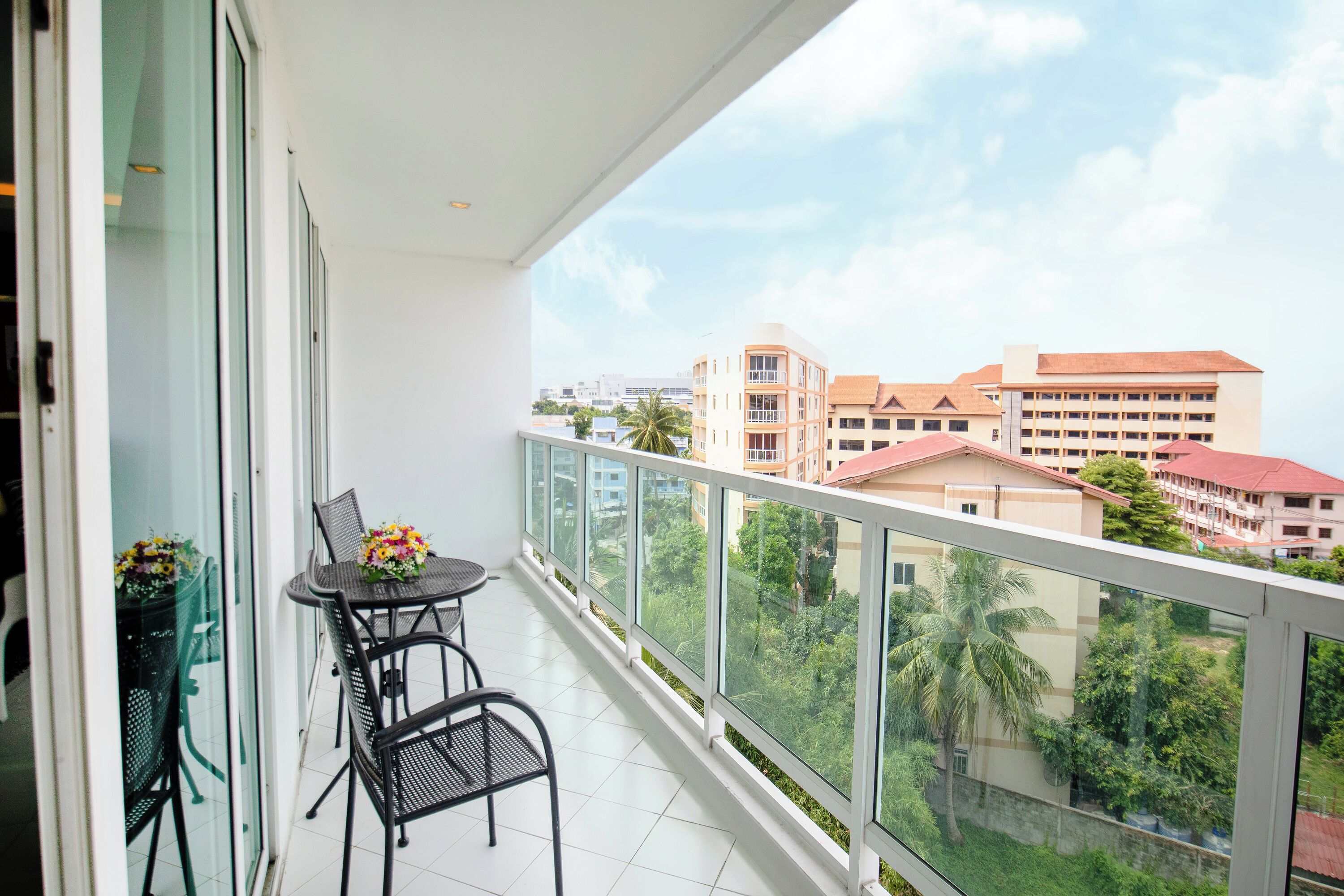 A balcony with a table and chairs, overlooking a residential area with buildings and greenery.