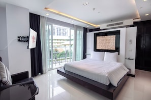 Une chambre d’hôtel moderne dotée d’un grand lit, d’un balcon offrant une vue sur les immeubles et d’un téléviseur à écran plat fixé au mur.