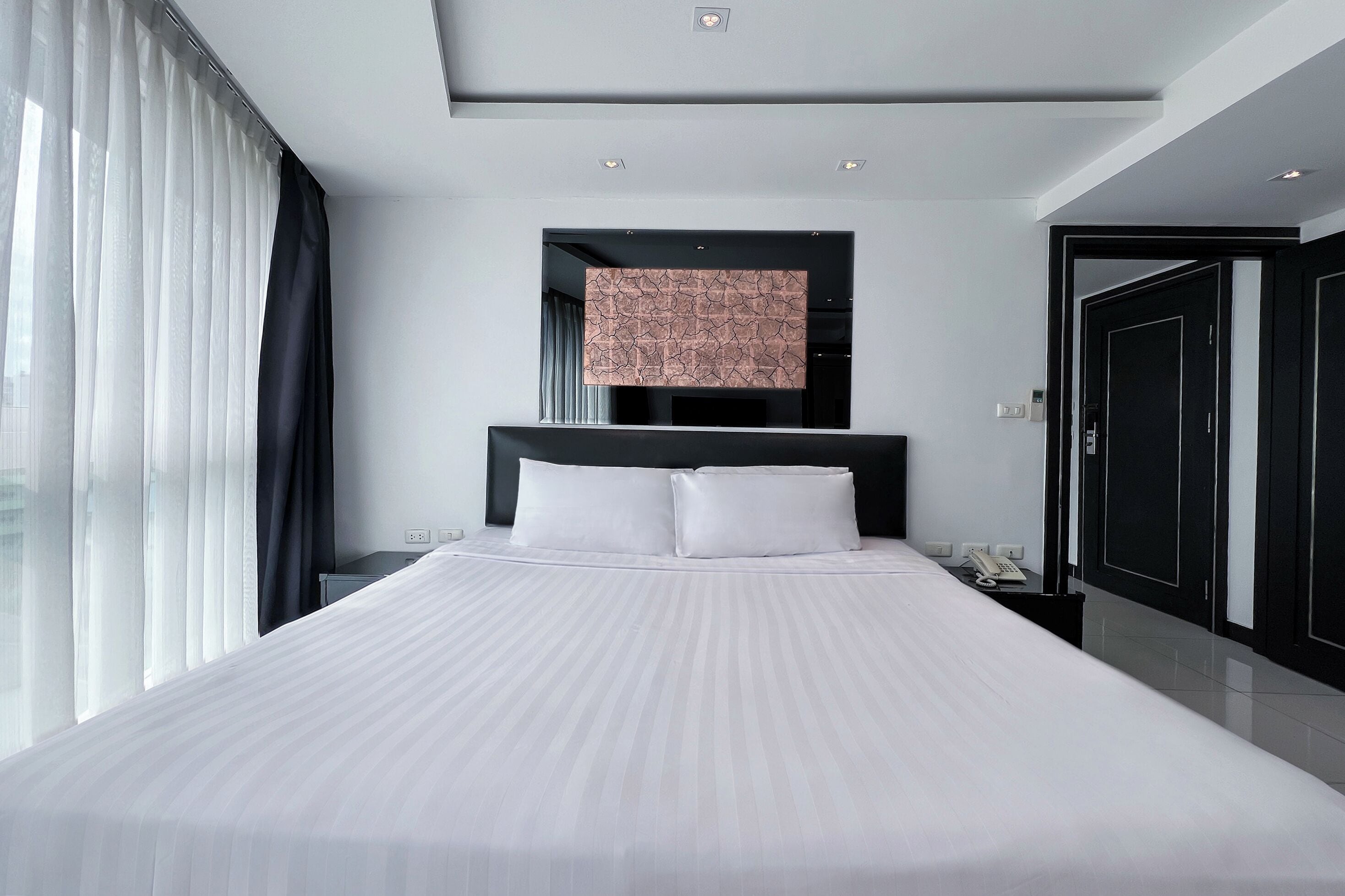 Una habitación de hotel moderna con una cama grande, una mesita de noche, un teléfono y una puerta.