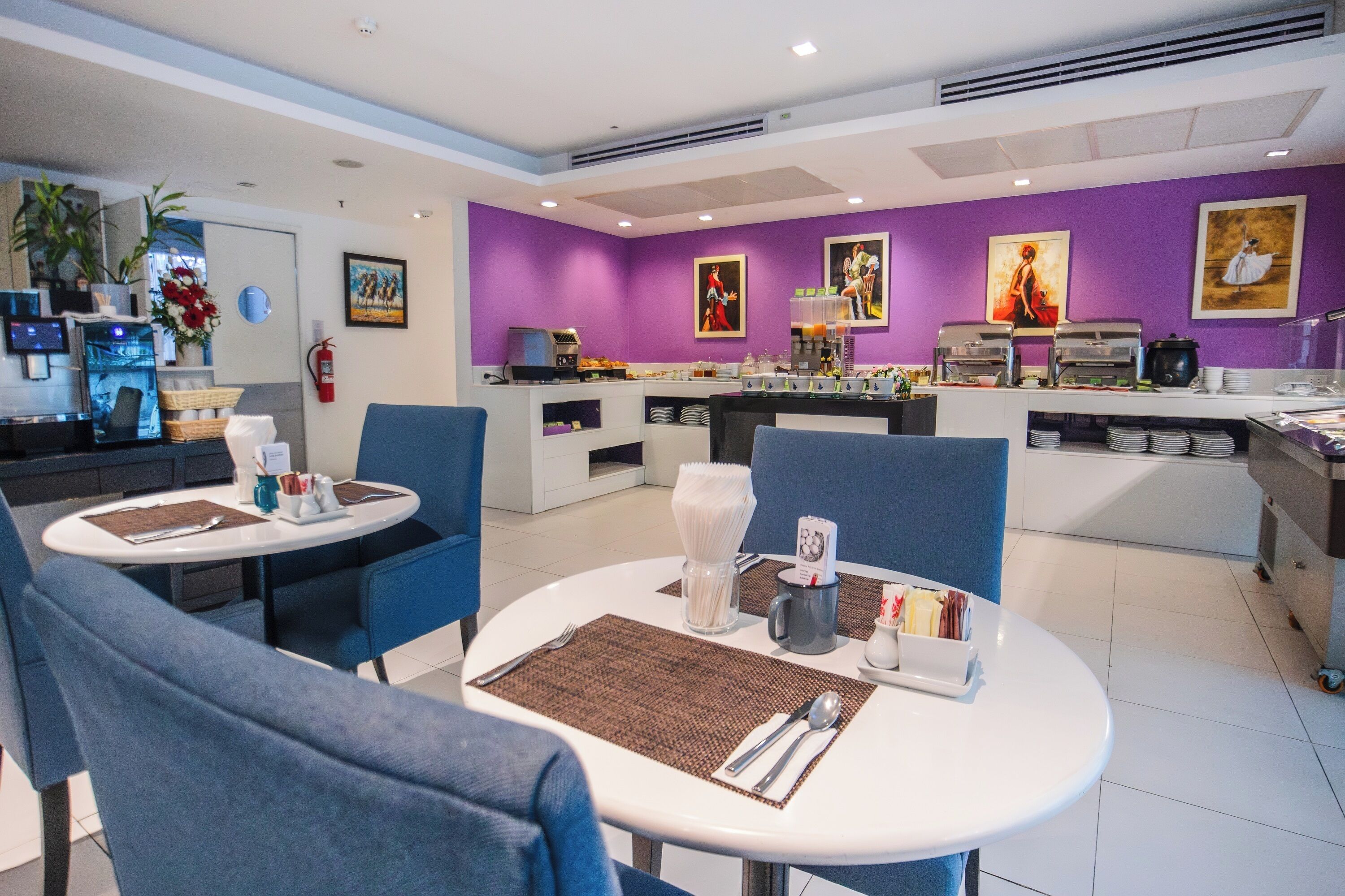 A hotel dining area with purple walls, a buffet setup, and blue chairs.