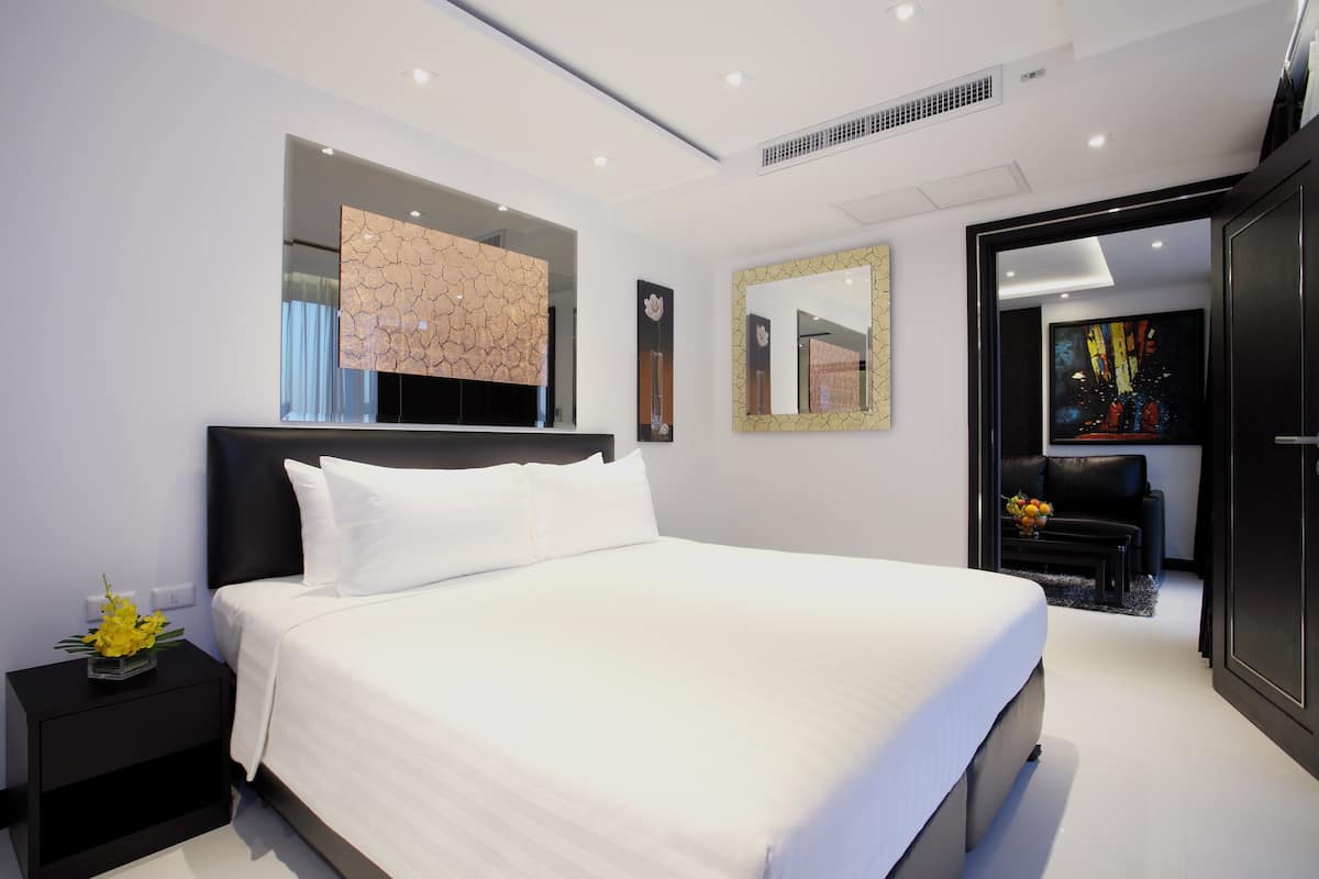 Un dormitorio moderno con una cama grande, una mesita de noche con un jarrón de flores, un espejo montado en la pared y un cuadro.