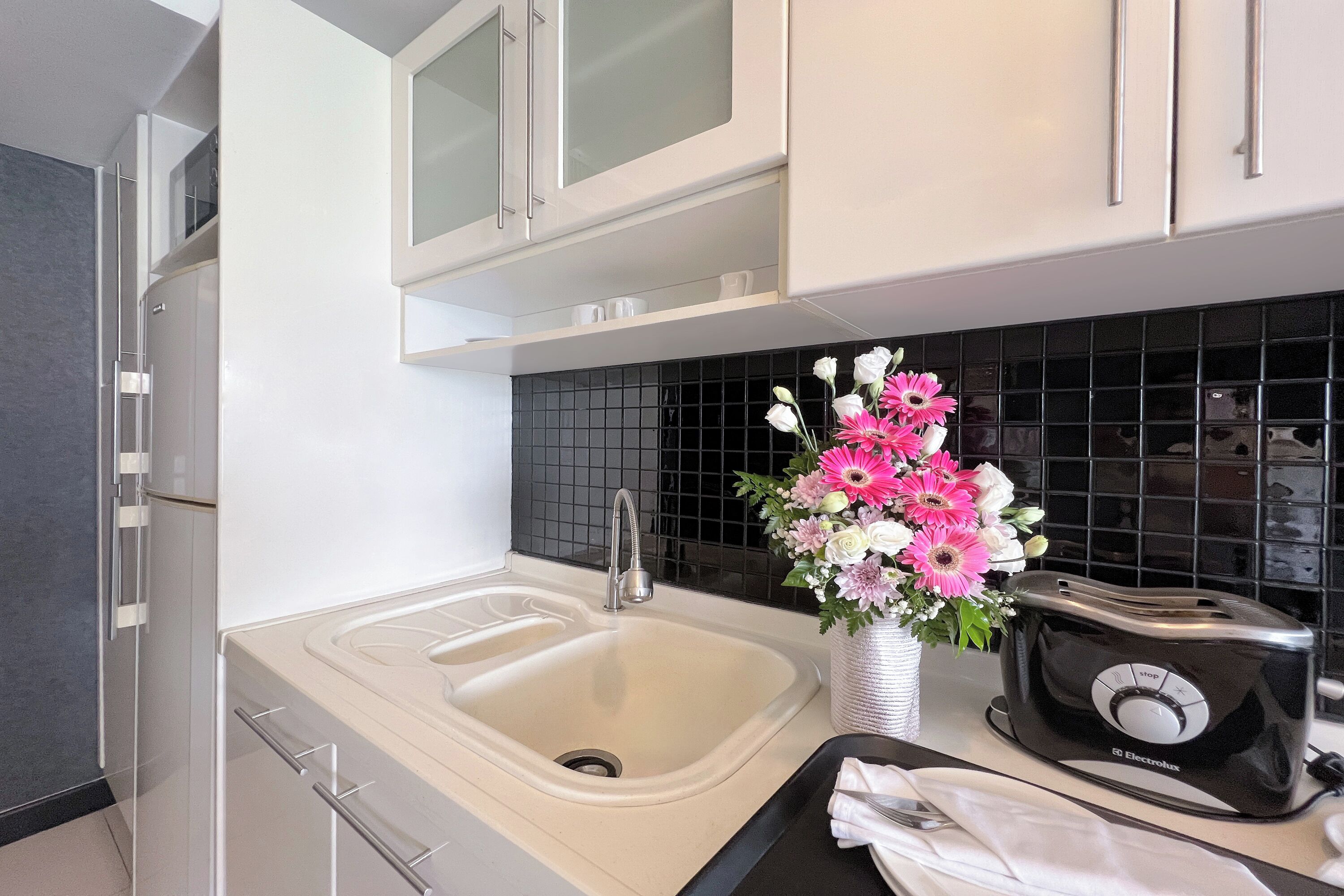A modern kitchen with a white sink, black backsplash, and a toaster.