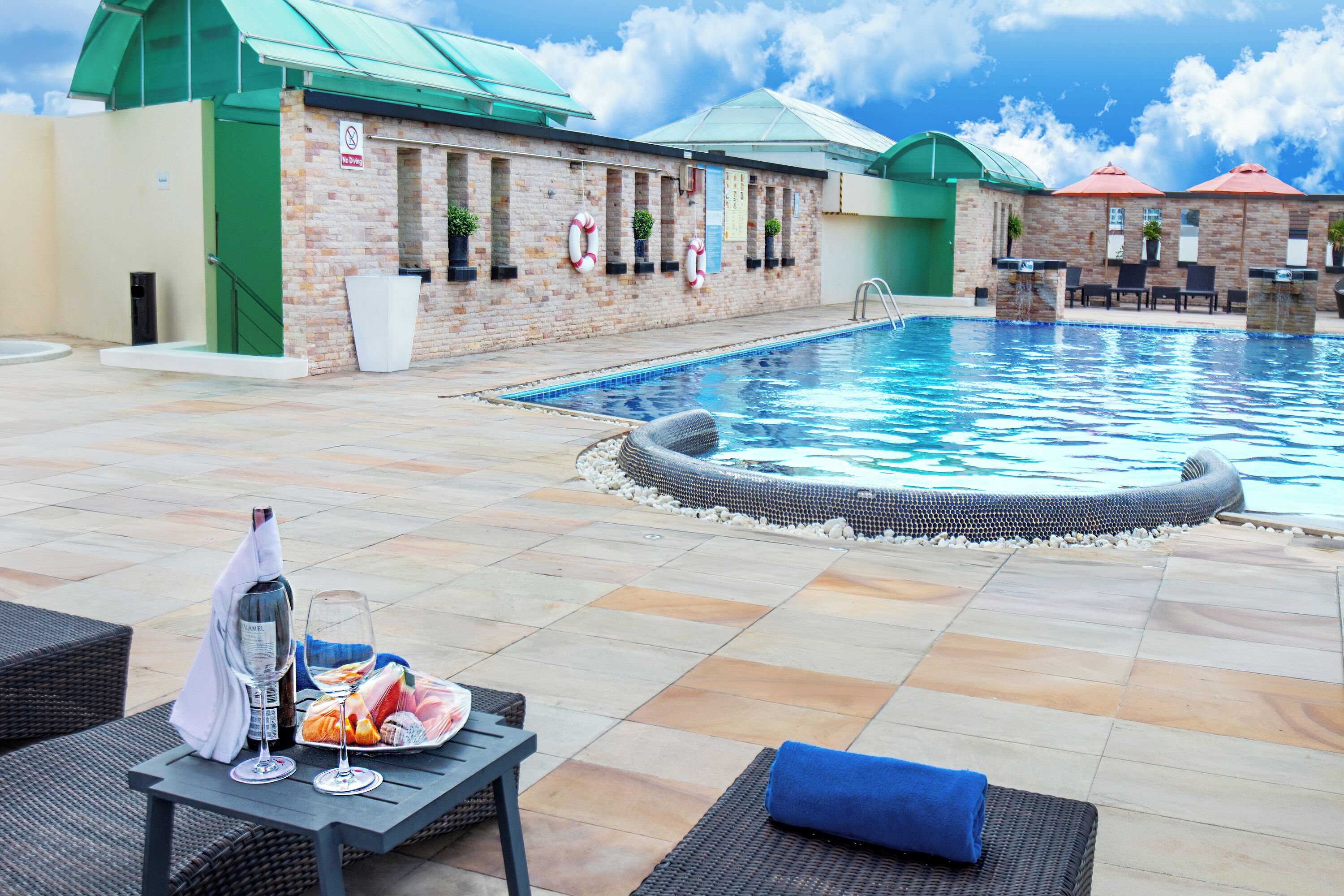 A pool area with a hot tub, lounge chairs, and a table with food and drinks.