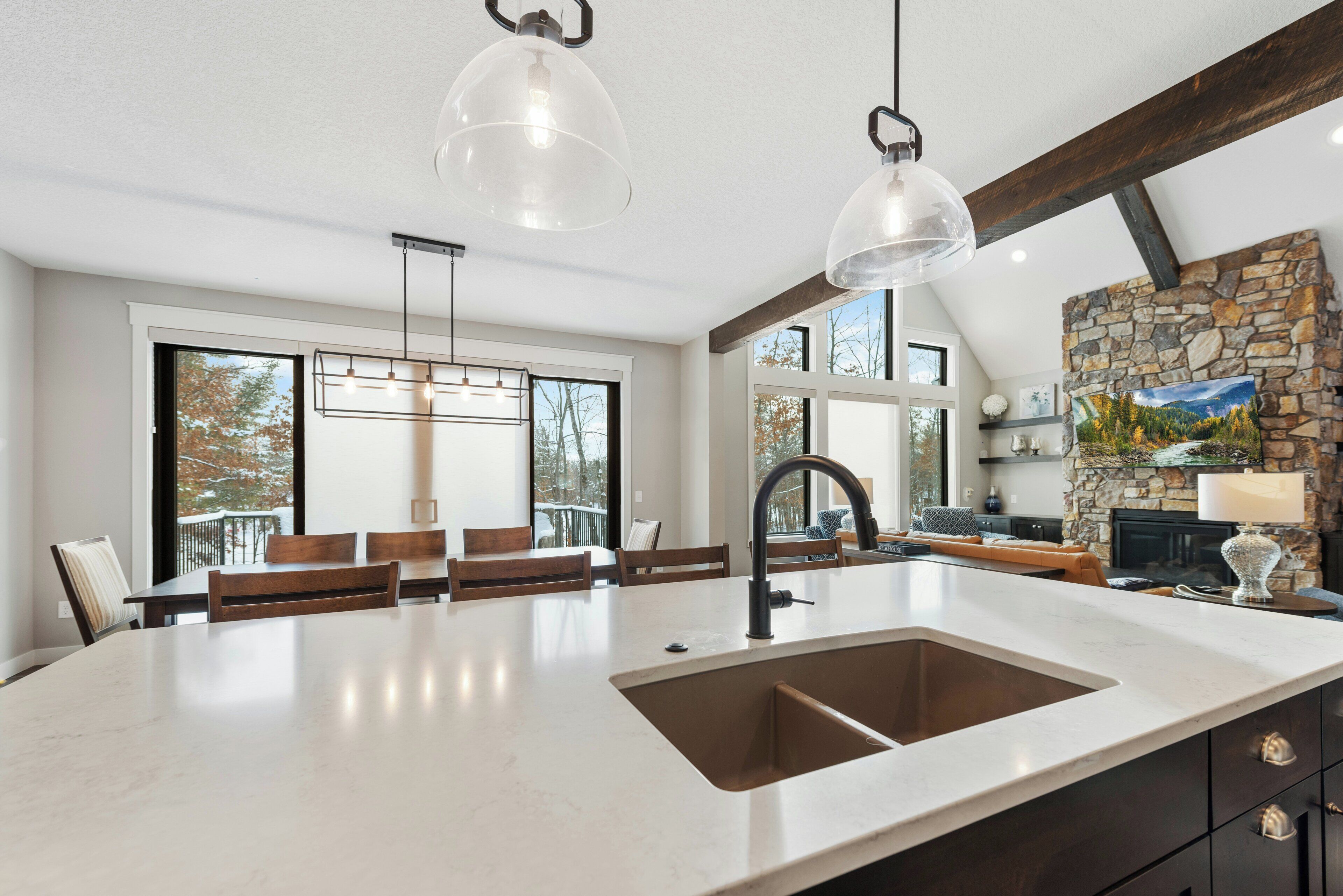 Een moderne keuken met een groot eiland, hanglampen en een accentmuur van steen.