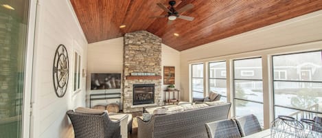 A covered outdoor seating area with wicker furniture, a stone fireplace, and a ceiling fan.