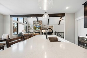 A spacious kitchen with a large island, dark wooden beams, a stone accent wall, and a pendant light.