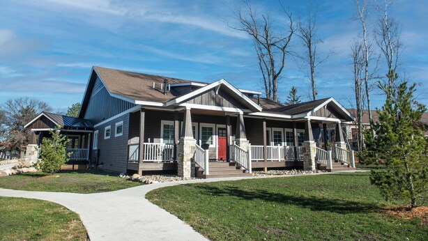 A modern two-story house with a covered porch, a stone foundation, and a well-maintained lawn.