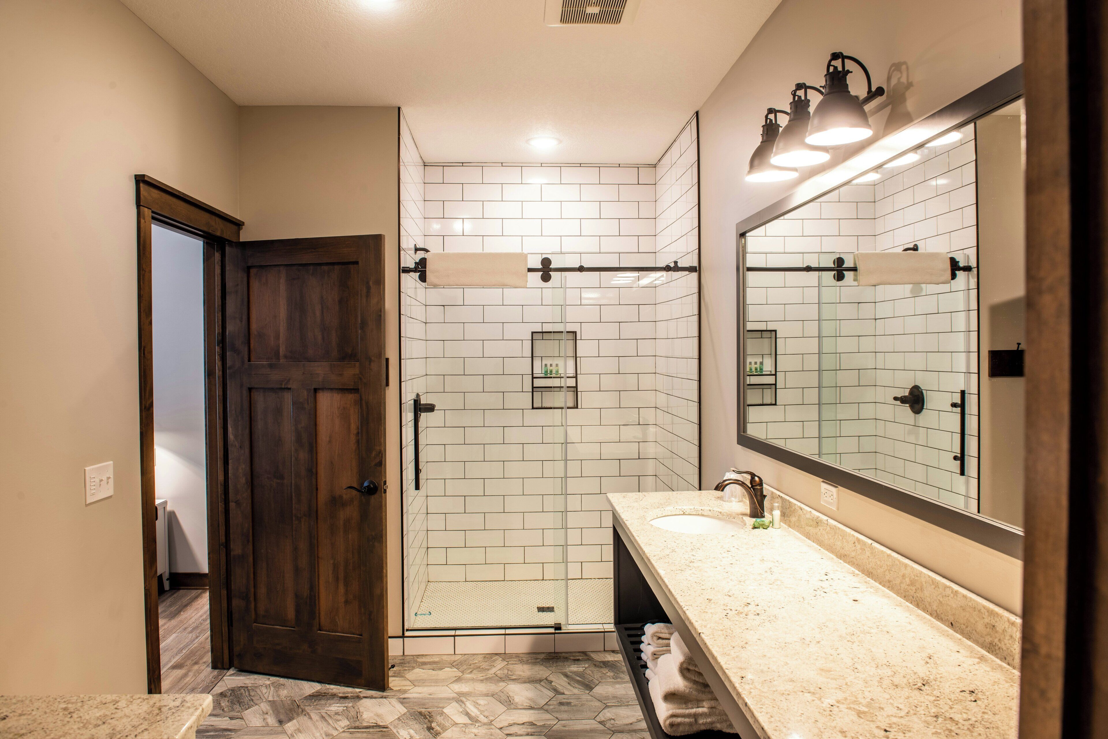 A bathroom with a wooden door, a shower with white tiles, a sink with a mirror, and a towel rack.
