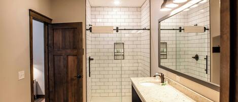 A bathroom with a wooden door, a shower with white tiles, a sink with a mirror, and a towel rack.