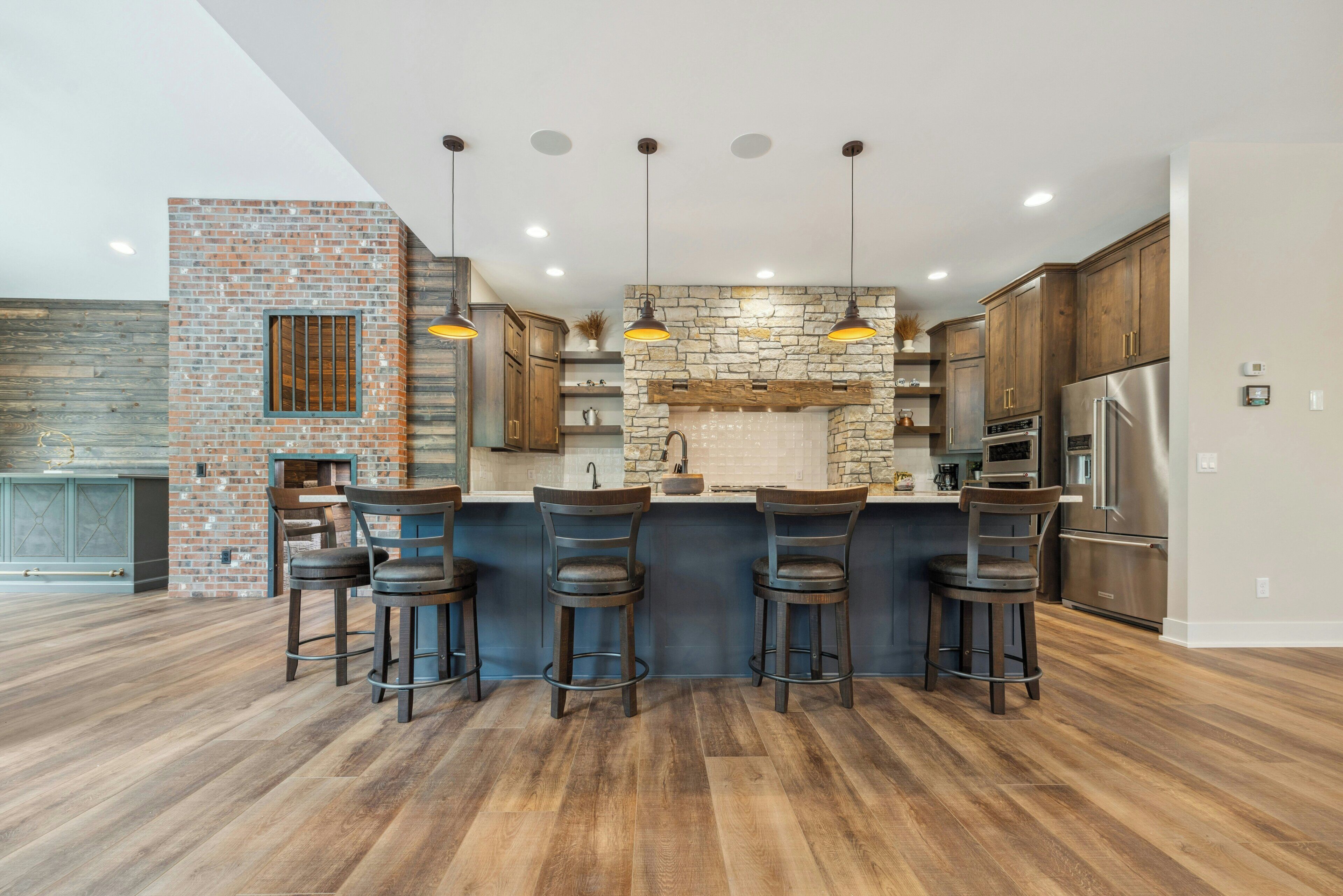 A modern kitchen with a brick accent wall, a stone backsplash, and a stainless steel refrigerator.