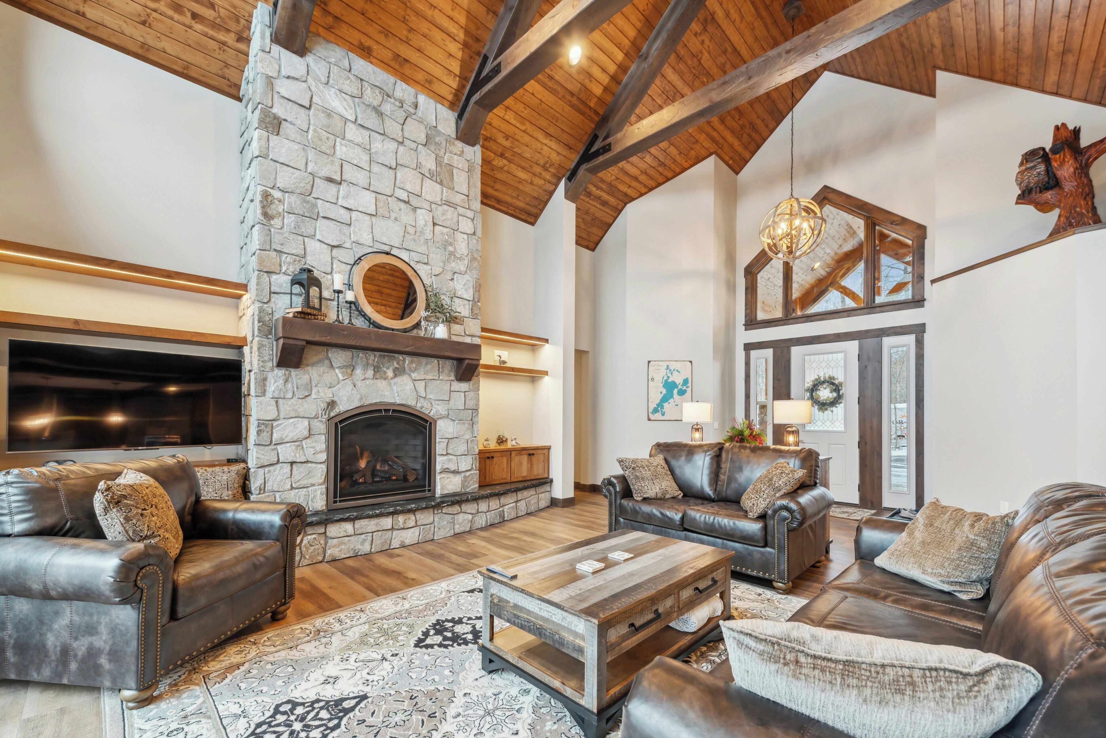 A spacious living room with a stone fireplace, leather sofas, a coffee table, and a high wooden ceiling.