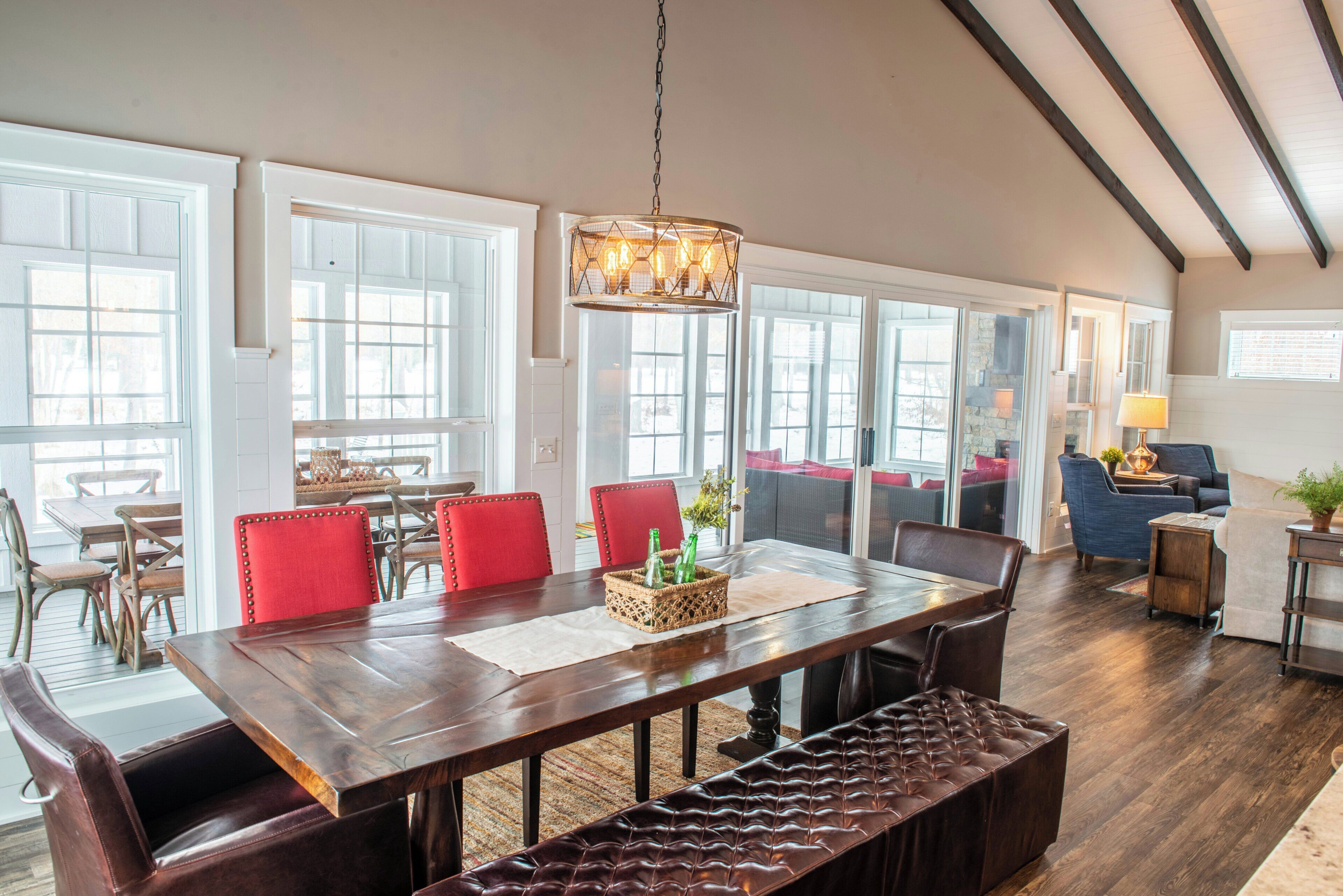 A spacious dining area with a long wooden table, red upholstered chairs, and a hanging light fixture.