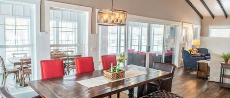 A spacious dining area with a long wooden table, red upholstered chairs, and a hanging light fixture.