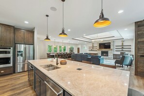 A modern kitchen with a large island, stainless steel appliances, and pendant lighting.