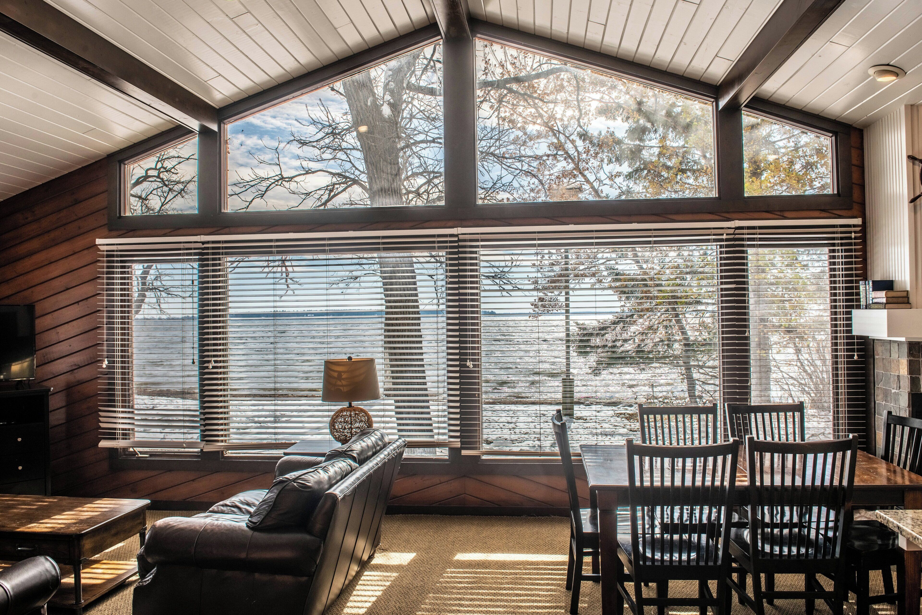 A room with a large bay window, a sofa, a dining table with chairs, and a lamp.