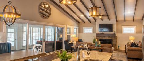 A spacious kitchen with a large island, a dining area with a long table, and a living room with a fireplace.